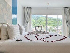 A hotel room with a bed, white curtains, and a view of greenery through large windows. - Patong Platinums (Patong)
