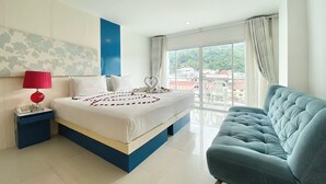 A hotel room with a large bed, a blue accent wall, a balcony with a view, and a blue sofa. - Patong Platinums (Patong)