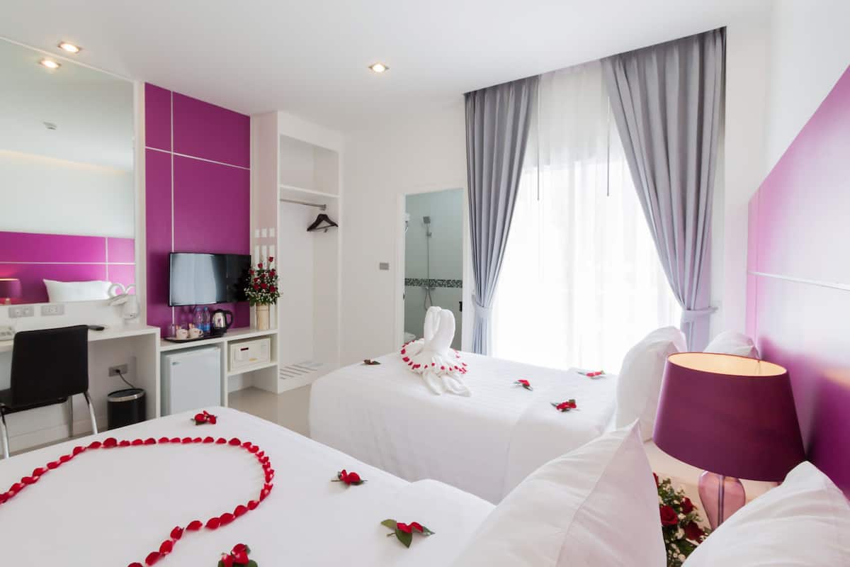 A hotel room with two beds, a desk, a TV, and a shower area.