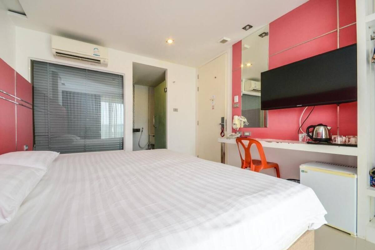 A bedroom with a bed, a desk, a chair, a mirror, and a small kitchenette.