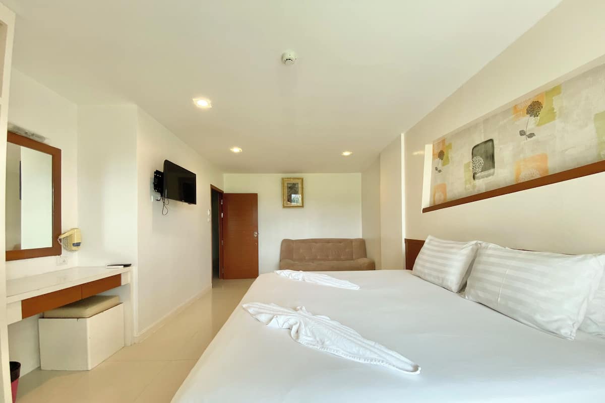 A hotel room with a large bed, a desk with a chair, a television, and a door leading to another room.
