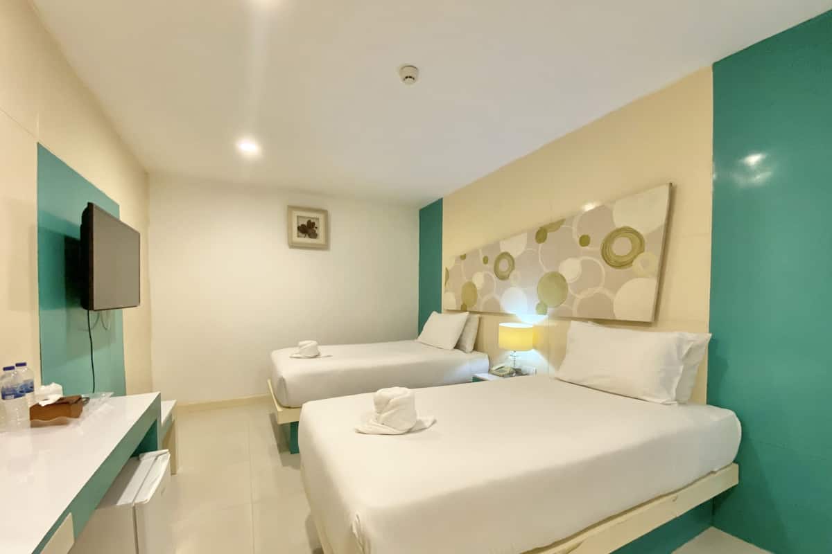 A hotel room with two beds, a desk, a television, and a wall with a circular pattern.