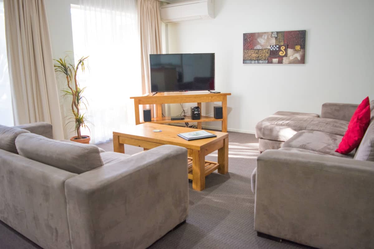 A living room with a flat-screen TV on a wooden stand, two sofas, a coffee table, and a potted plant.