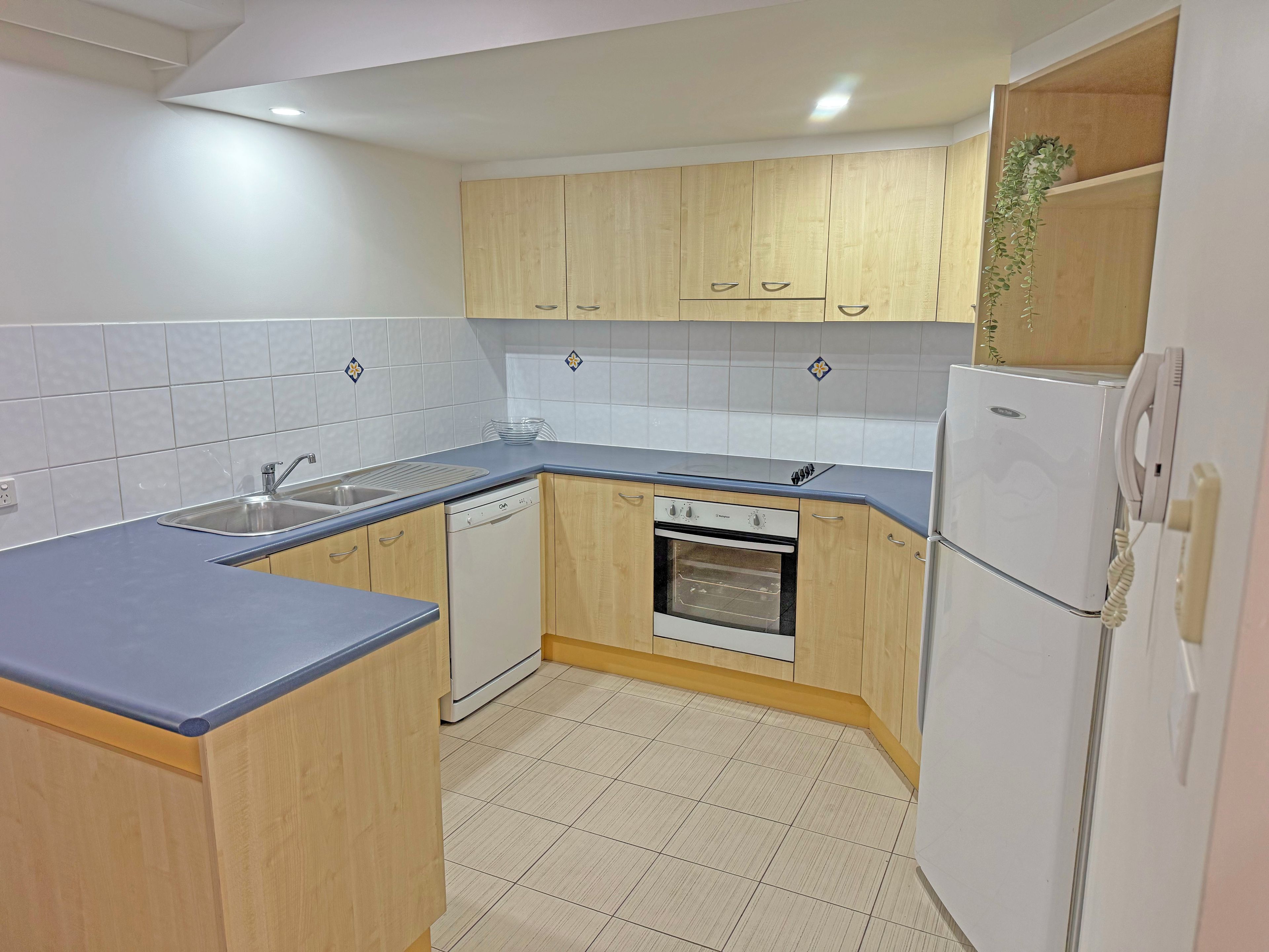 A kitchen with wooden cabinets, a dishwasher, an oven, a refrigerator, and a sink.