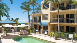A multi-story hotel with balconies, a swimming pool, and palm trees. - Beachside Holiday Apartments (Port Macquarie)
