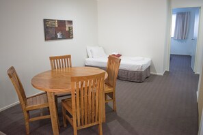 A room with a round wooden table and four chairs, a bed with white bedding, and a painting on the wall. - Beachside Holiday Apartments (Port Macquarie)