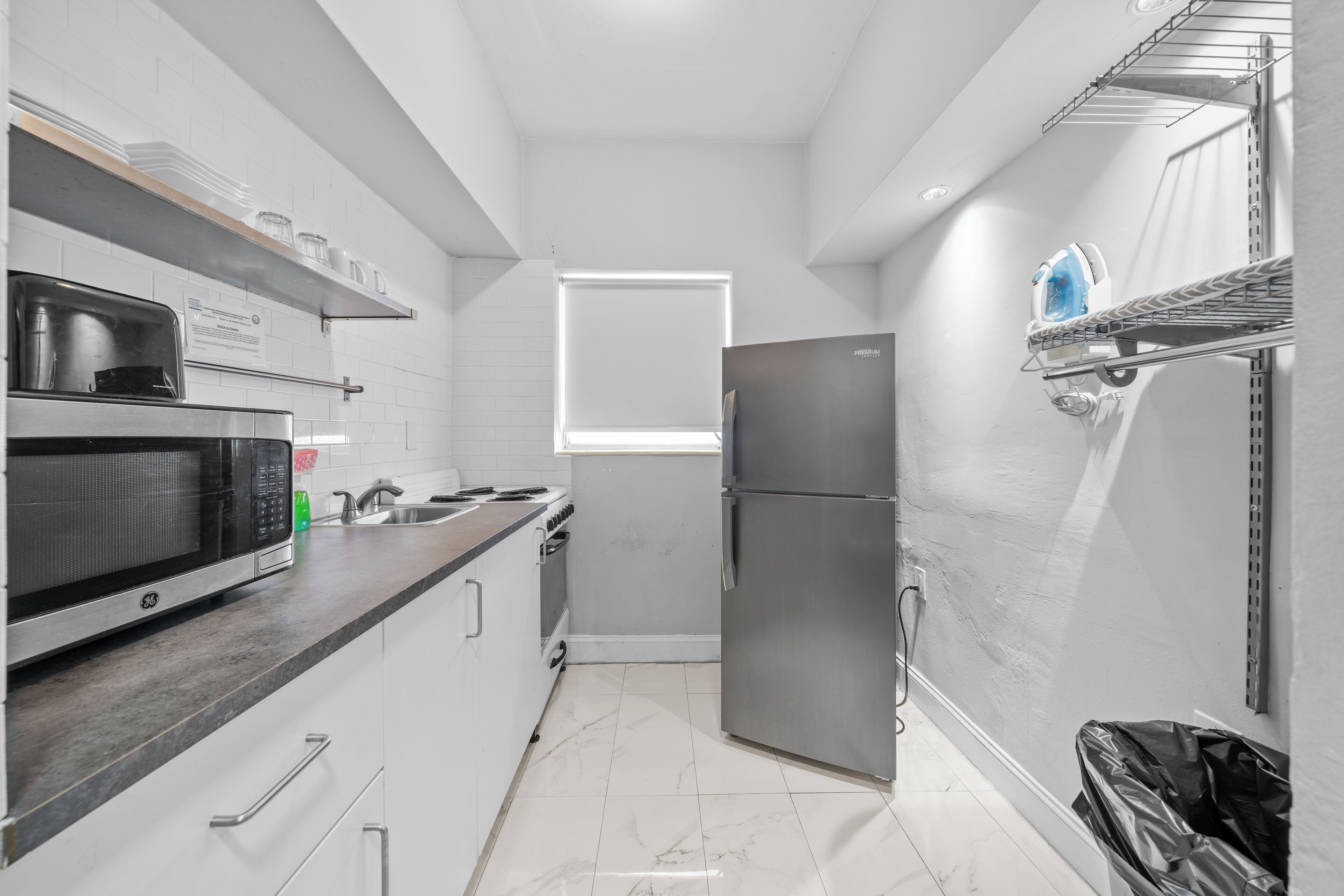 Una cocina moderna con armarios blancos, un refrigerador de acero inoxidable, un microondas y un lavamanos.