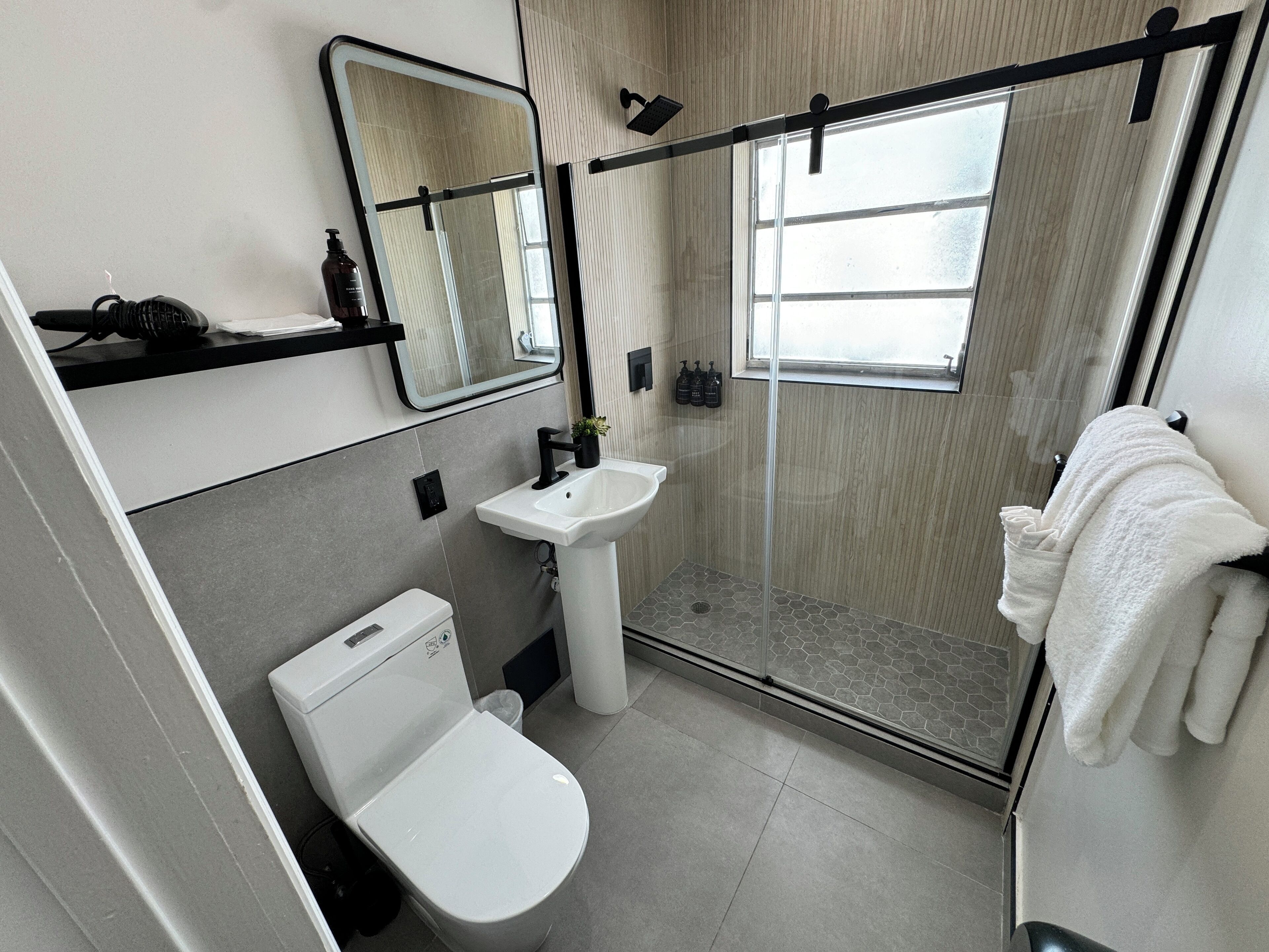 A modern bathroom with a toilet, sink, shower, and a large mirror.