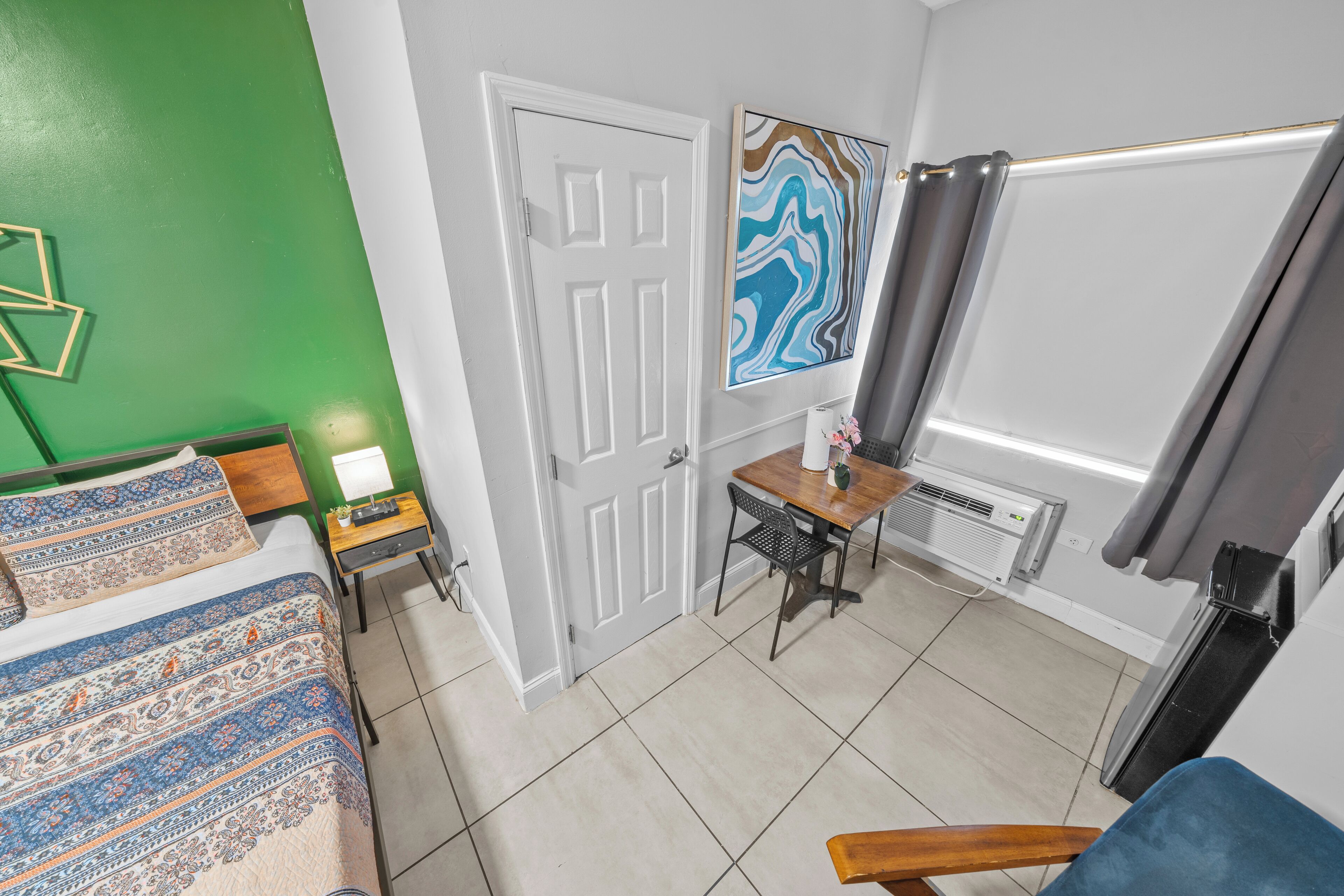 A bedroom with a bed, a desk, a chair, a radiator, and a door.