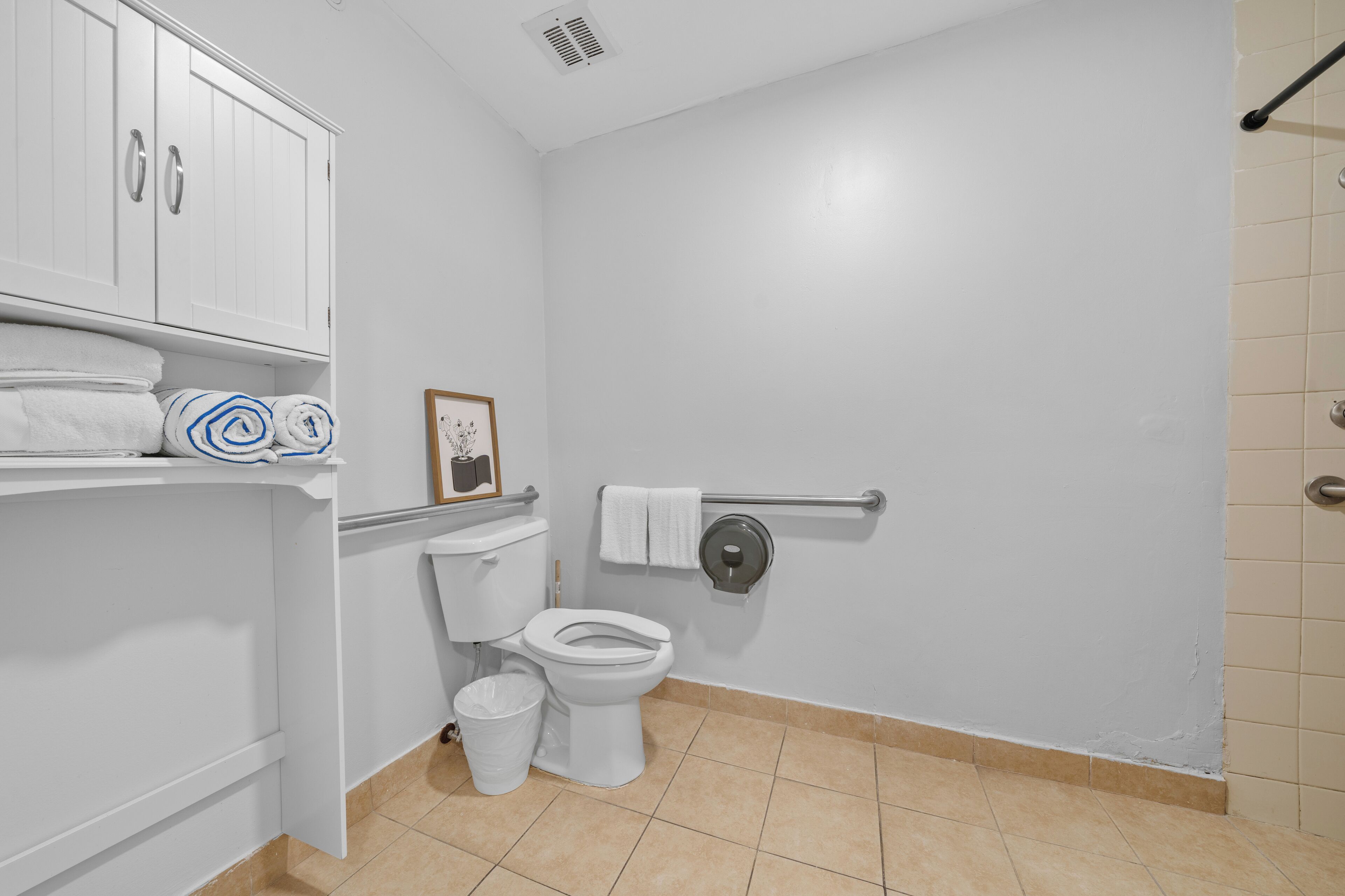 Een badkamer met een toilet, een prullenbak, een handdoekhouder en een plank met handdoeken.