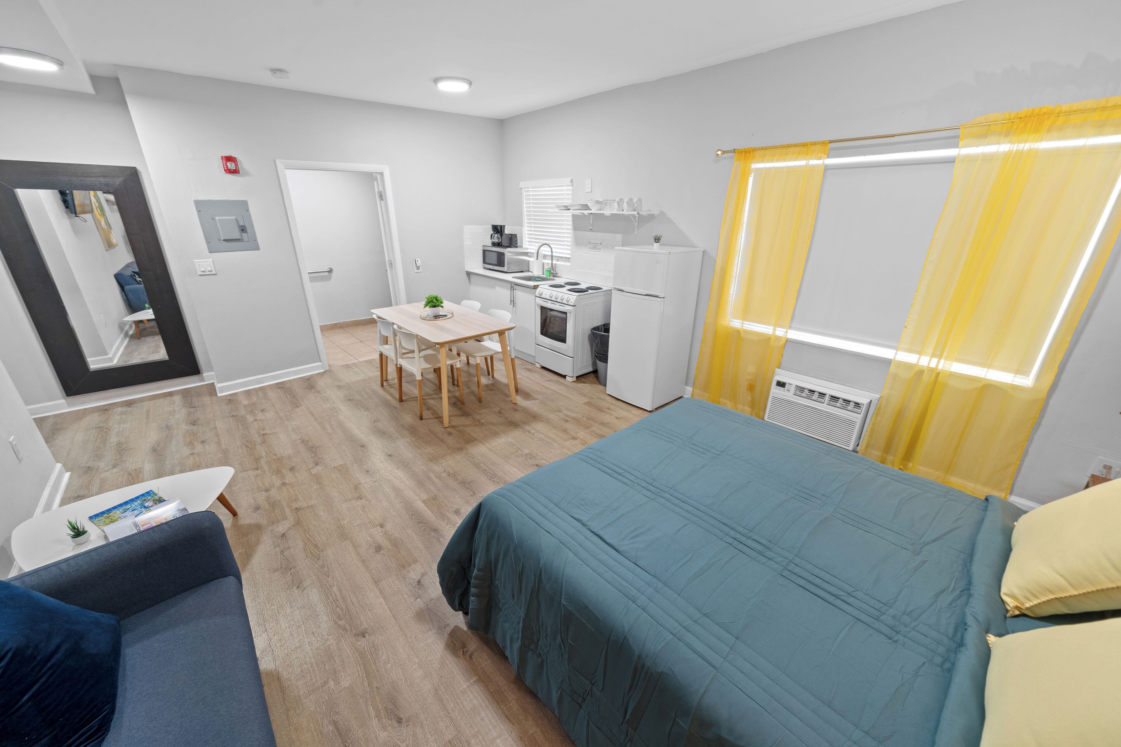 Une chambre d’hôtel de taille réduite, comprenant un lit, un petit bureau avec une chaise, une kitchenette et une salle de bain.
