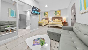 A modern hotel room with a sofa, a bed with yellow bedding, a small table with a magazine, and a TV on the wall. - Miami International by Lowkl (Miami Beach)