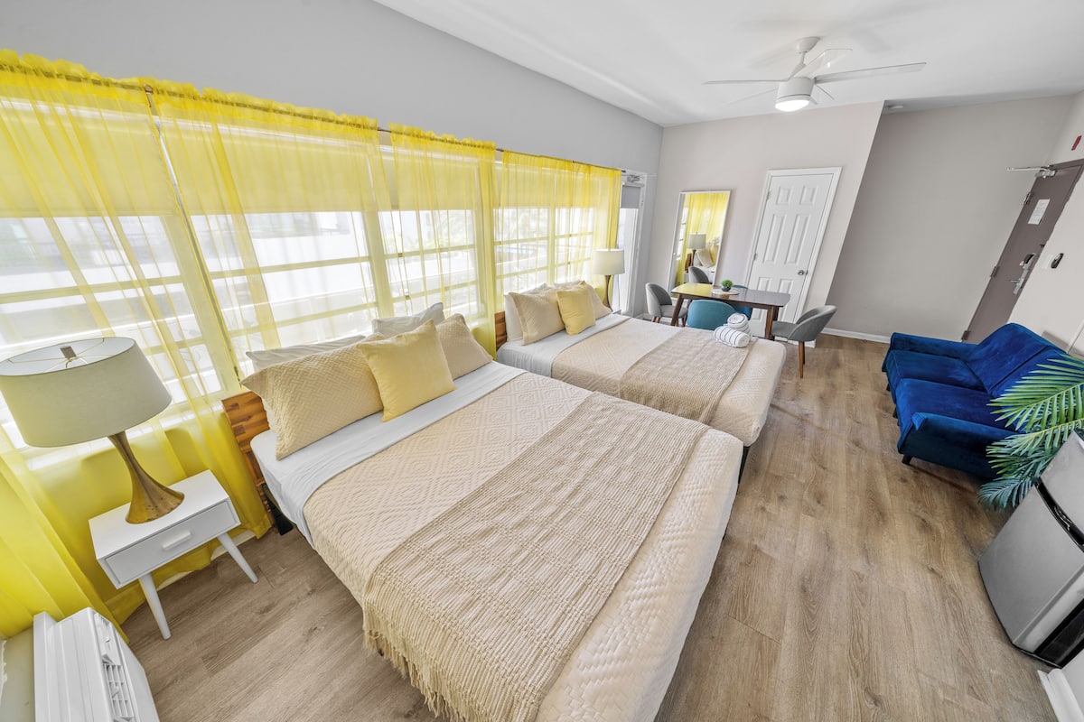 A hotel room with two beds, a desk, a chair, a mirror, and a blue sofa.