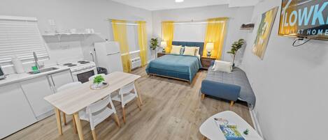 A modern, well-lit room with a bed, bedside table, and a small seating area.