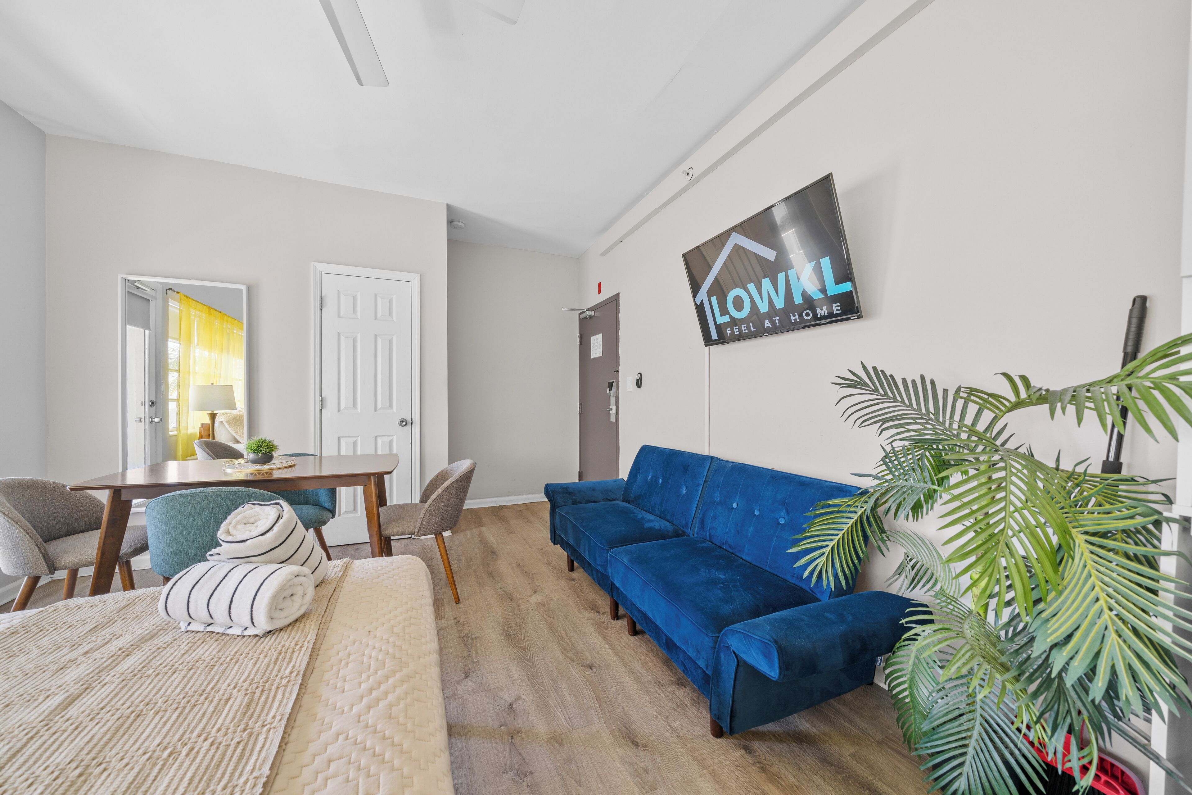 A modern living room with a blue sofa, a dining table with chairs, a large mirror, and a potted plant.
