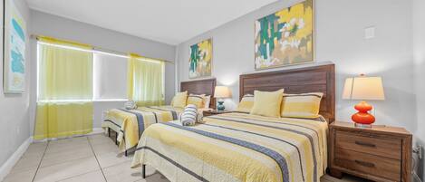 A hotel room with two beds, a nightstand with a lamp, and artwork on the walls.