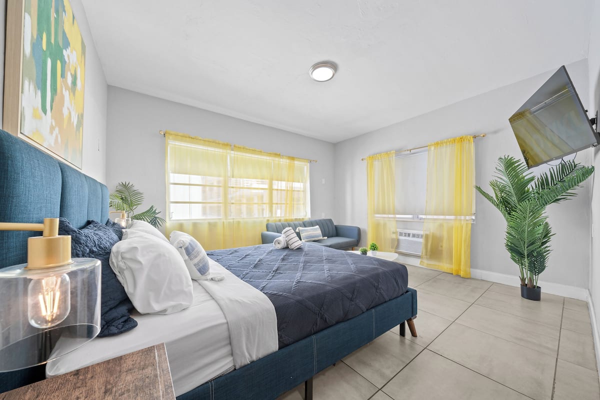 A modern bedroom with a bed, bedside table, and a large window with yellow curtains.