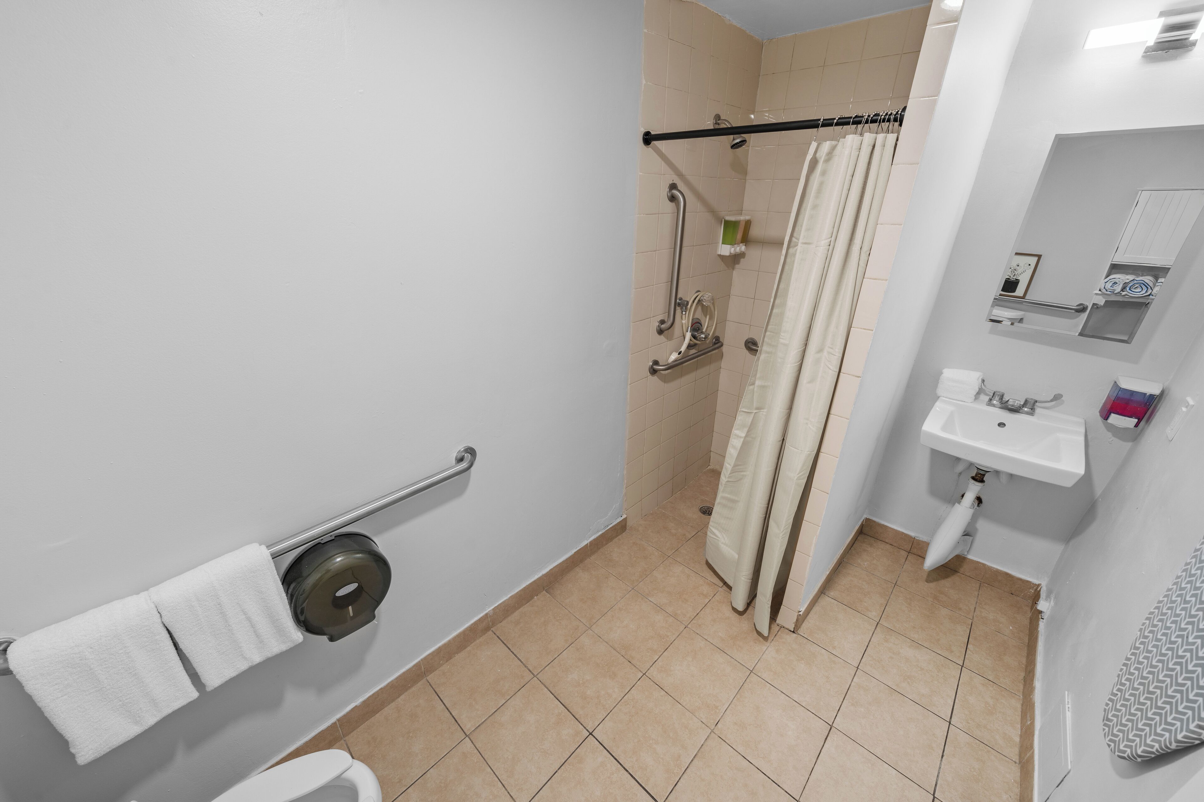 Une salle de bain comprenant des toilettes, un lavabo, une douche équipée d’une barre d’appui et un porte-serviettes.