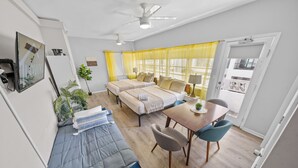 A modern, well-lit room with a sofa, two beds, a dining table, and a ceiling fan. - Miami International by Lowkl (Miami Beach)