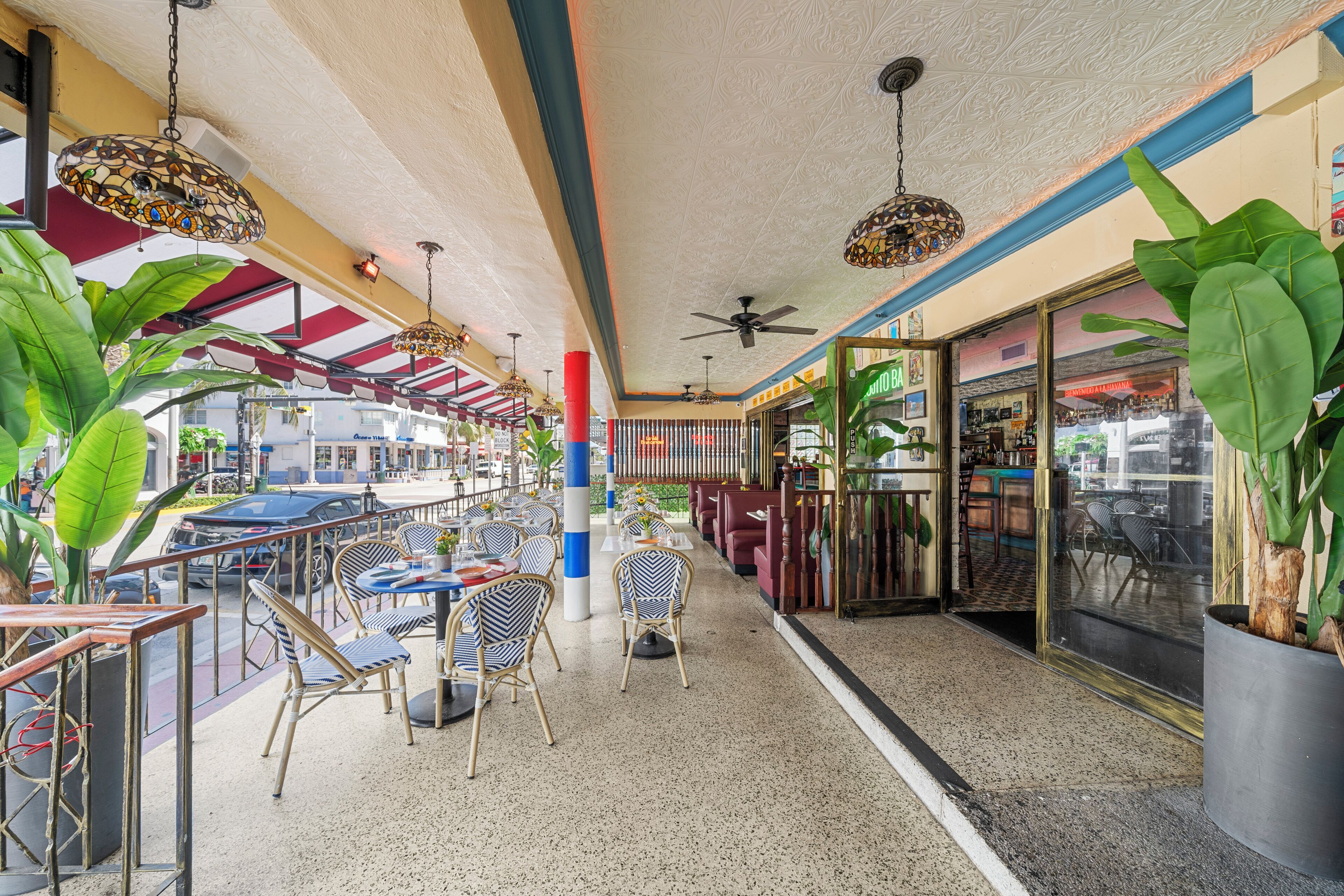 An indoor dining area with tables and chairs, ceiling fans, and large potted plants.