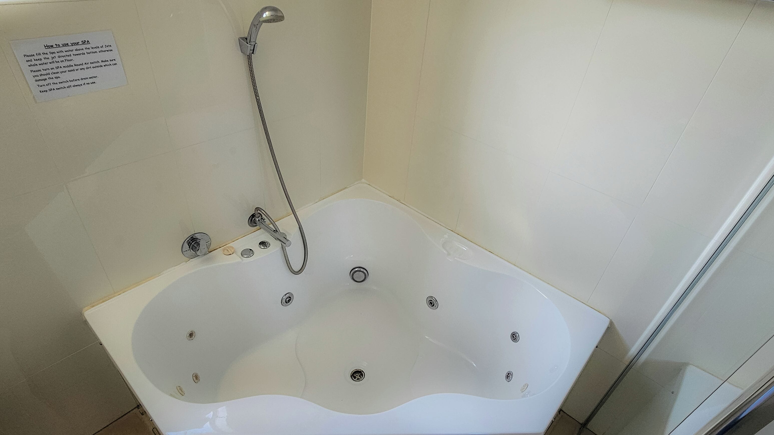Una bañera de spa blanca con ducha y panel de control, un cartel con instrucciones de uso y una pared de azulejos.