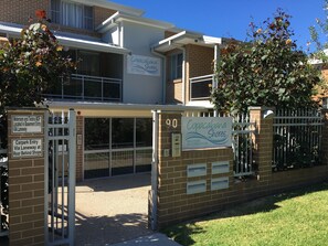 Un edificio con un letrero que dice "Copacabana Shores", indicando un alojamiento frente a la playa. Tiene varios accesos, incluyendo una entrada con puerta y un estacionamiento.