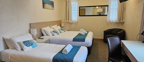 Ein Hotelzimmer mit zwei Betten, einem Schreibtisch, einem Stuhl, einem Fernseher und einem Bild an der Wand.