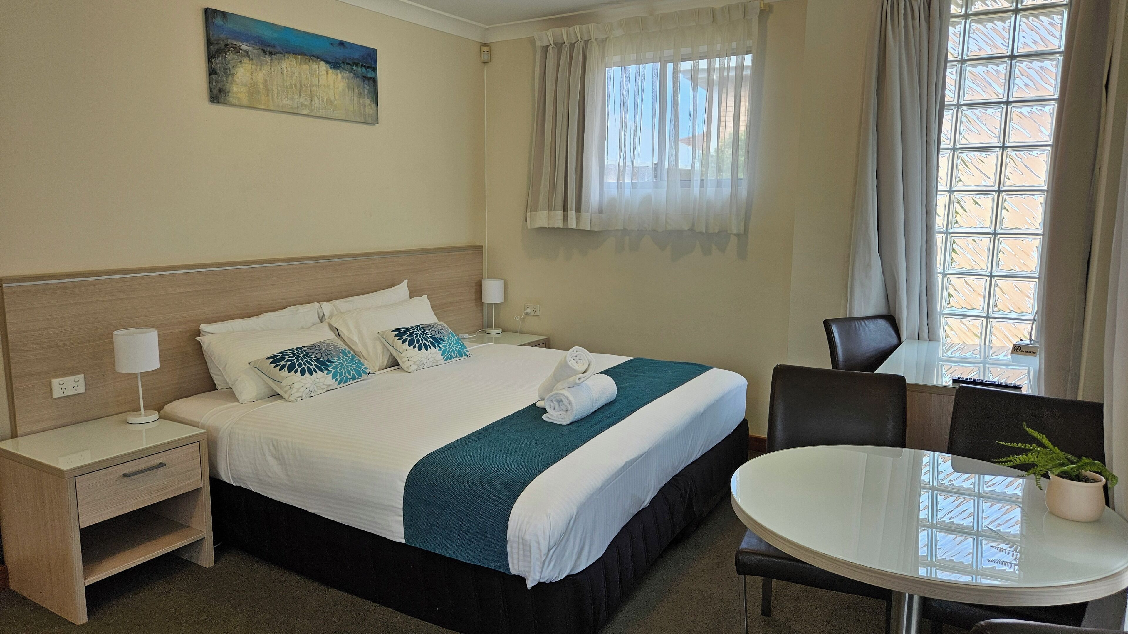 A hotel room with a bed, bedside tables, a chair, a small table with a plant, and a window with curtains.
