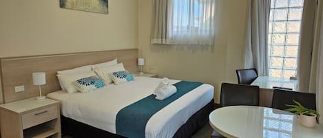 A hotel room with a bed, bedside tables, a chair, a small table with a plant, and a window with curtains.