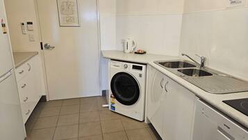 A compact laundry room with a front-loading washing machine, a sink, and a small countertop with a kettle.