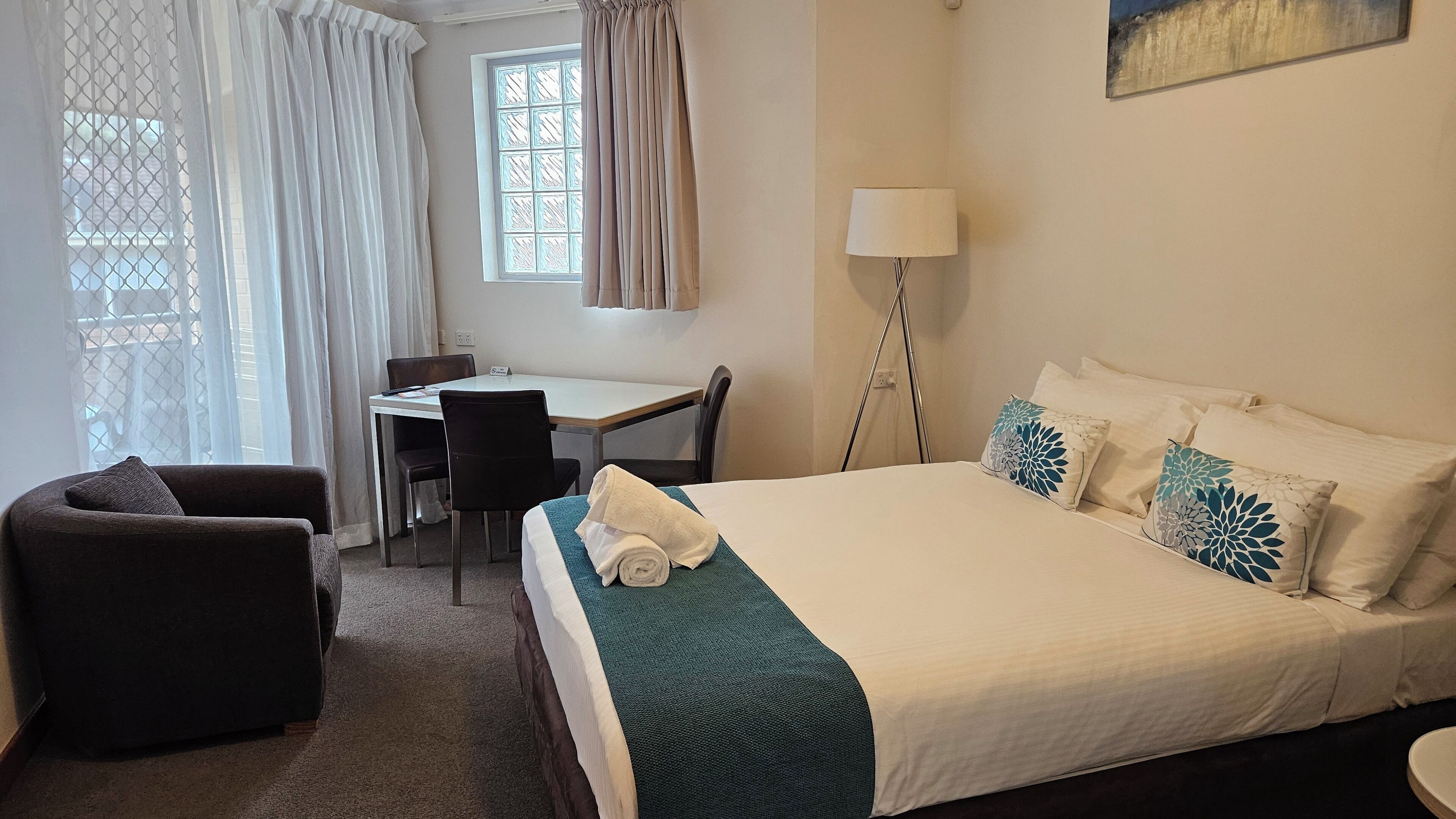 A hotel room with a bed, a desk, a chair, a sofa, and a lamp.