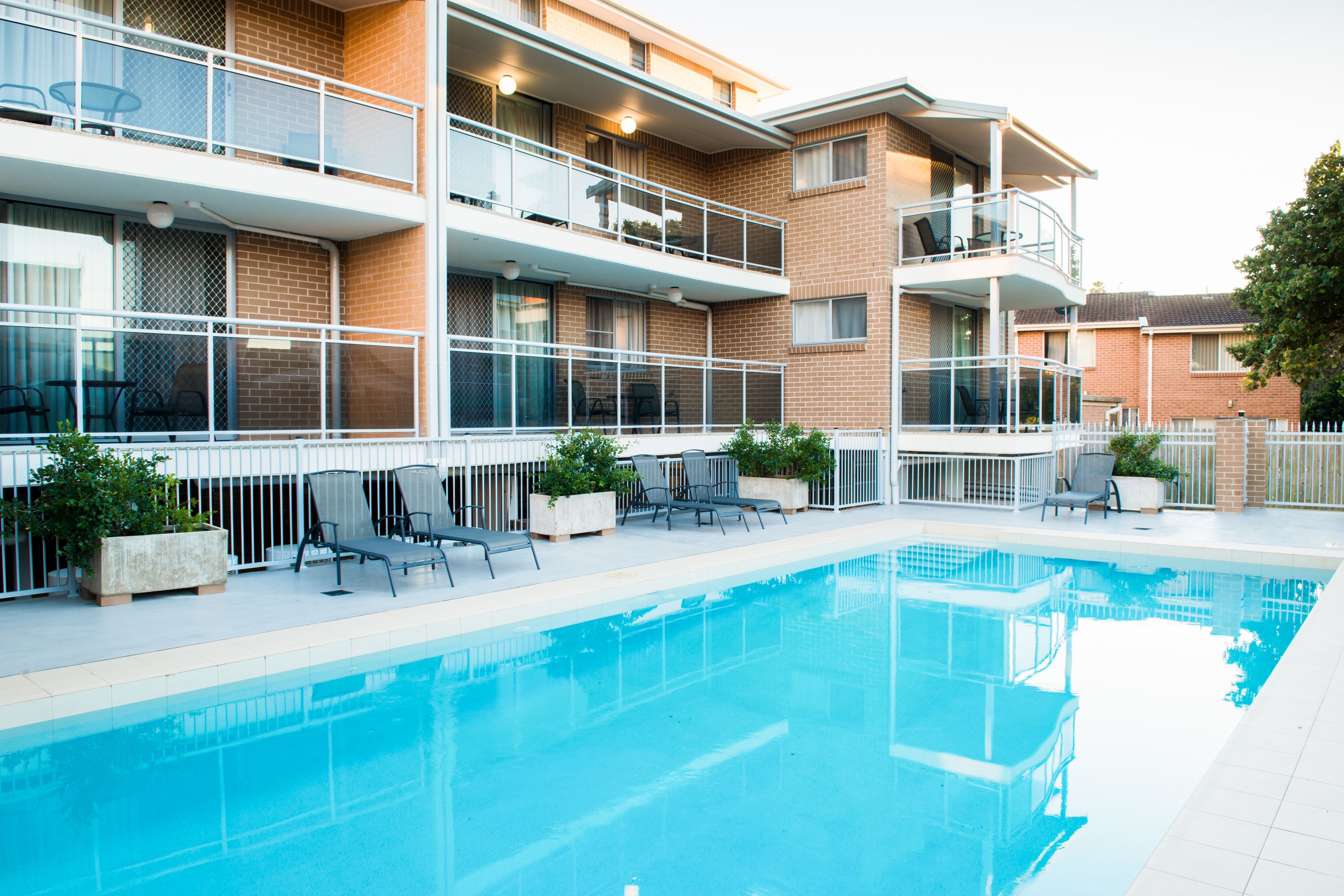 A modern apartment building with a swimming pool, outdoor seating, and a fenced balcony area.