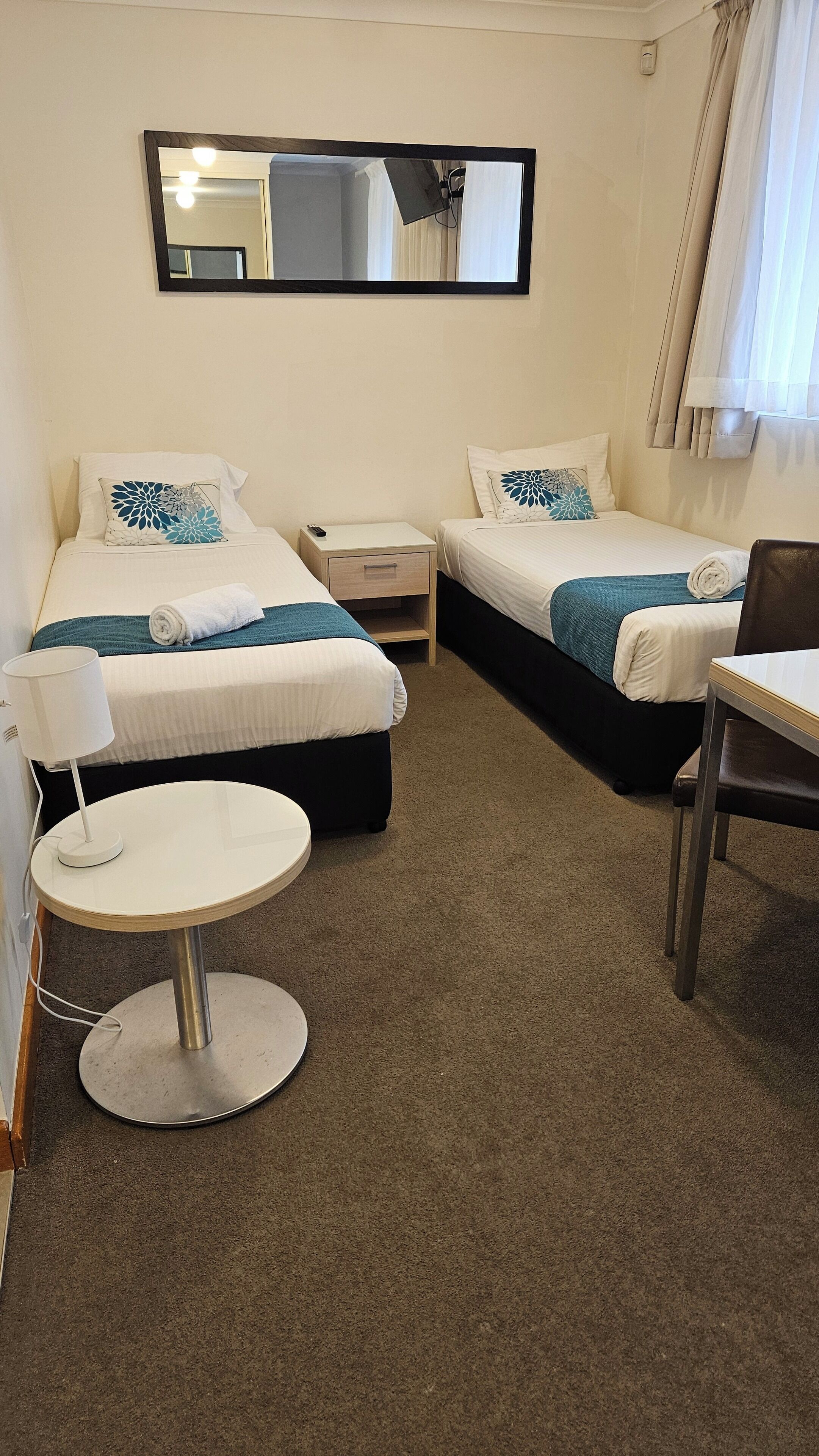 A hotel room with two beds, a round table, a chair, a nightstand, and a mirror on the wall.