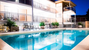 A swimming pool with lounge chairs and potted plants, surrounded by a white fence and a two-story building with balconies. - Copacabana Shores (Copacabana)