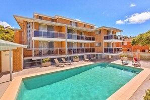 Un edificio residencial de varios pisos con piscina, mobiliario exterior y un área de balcón cercada.