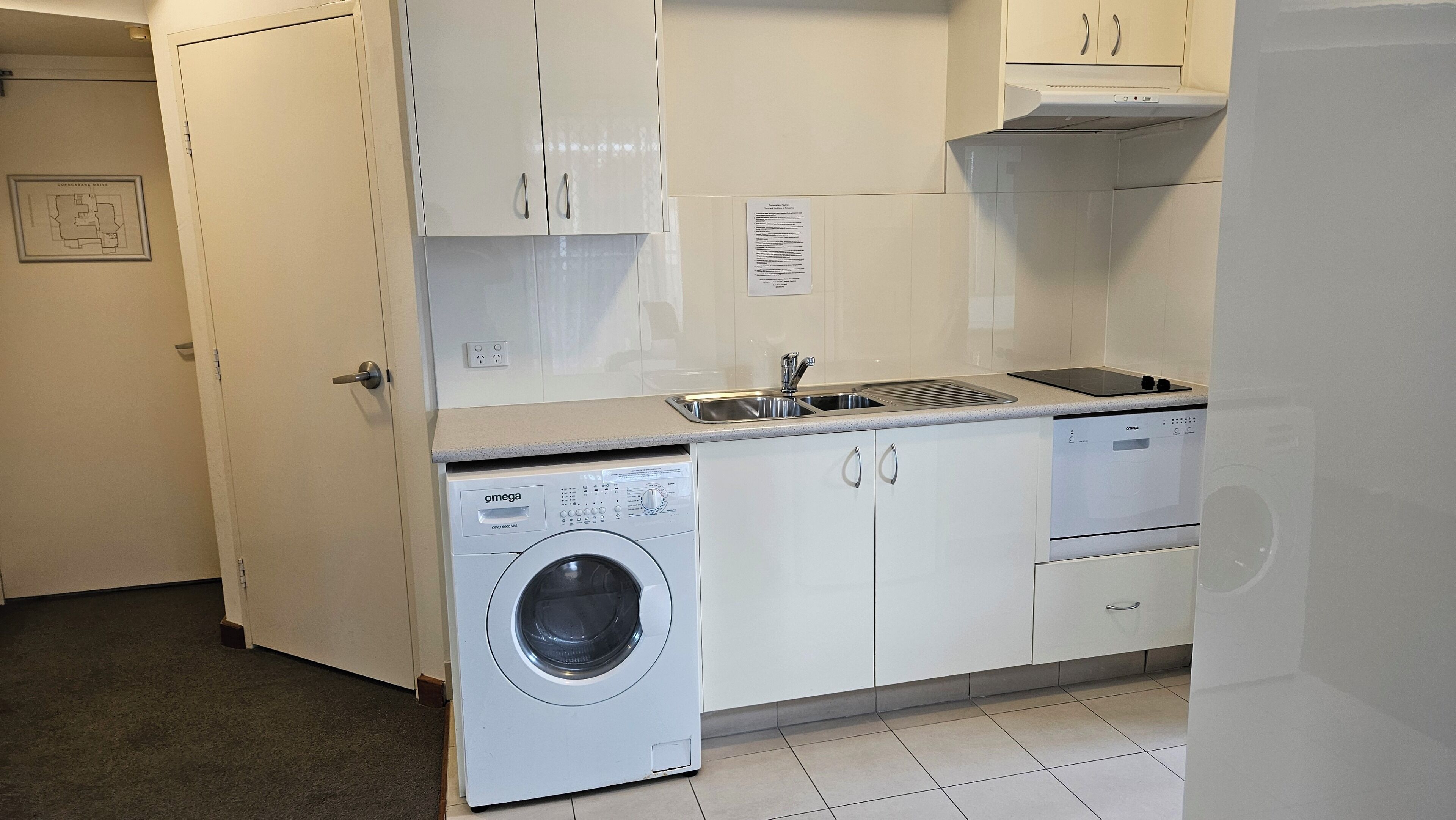 A compact kitchen with a built-in washer and dryer, a sink, and white cabinets.