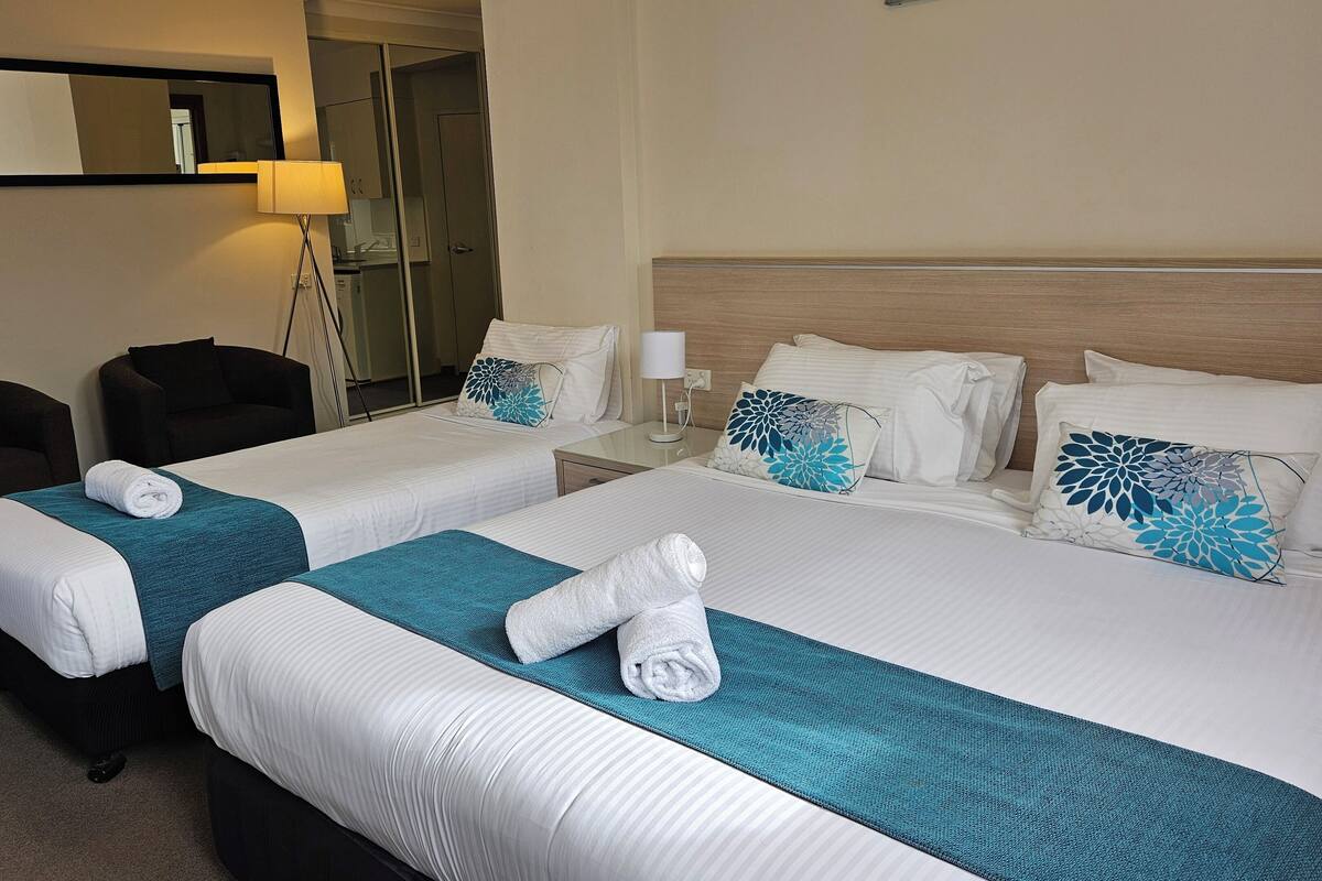 Quarto de hotel com duas camas, um sofá, um espelho e um abajur.