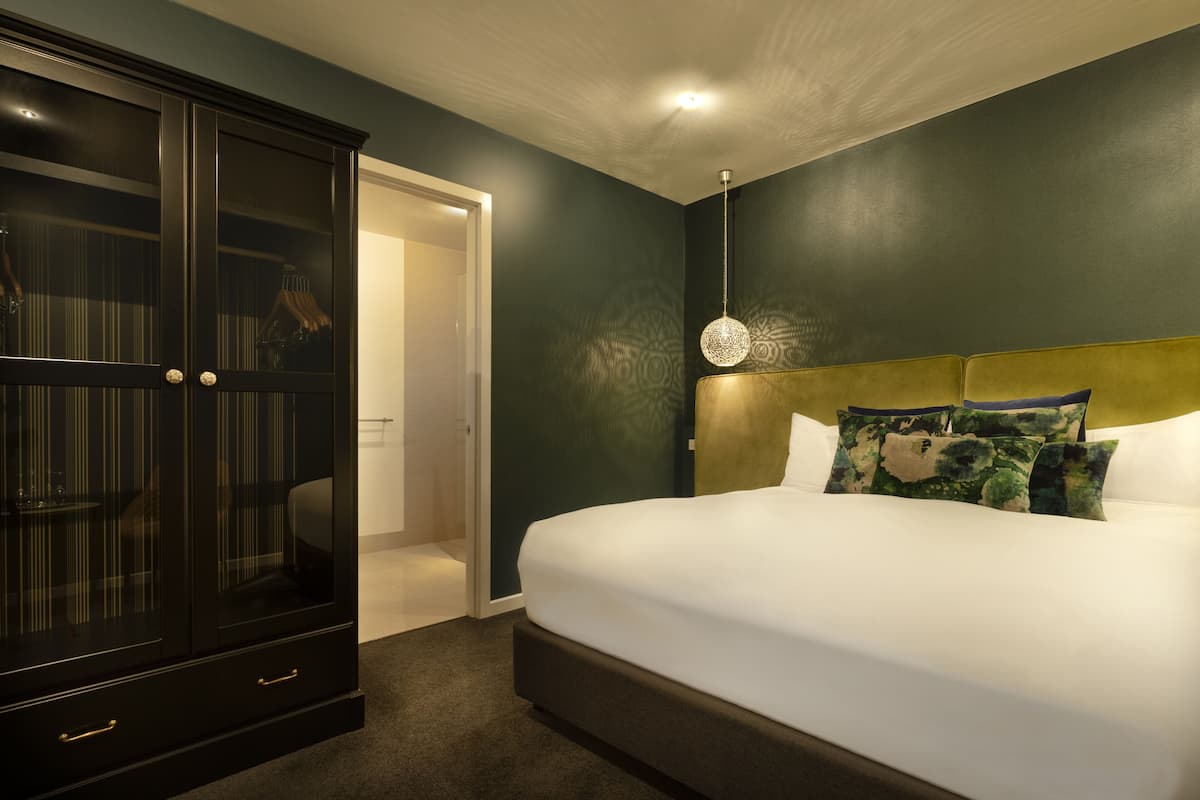 A bedroom with a large bed, a dark wooden wardrobe, and a patterned wall.