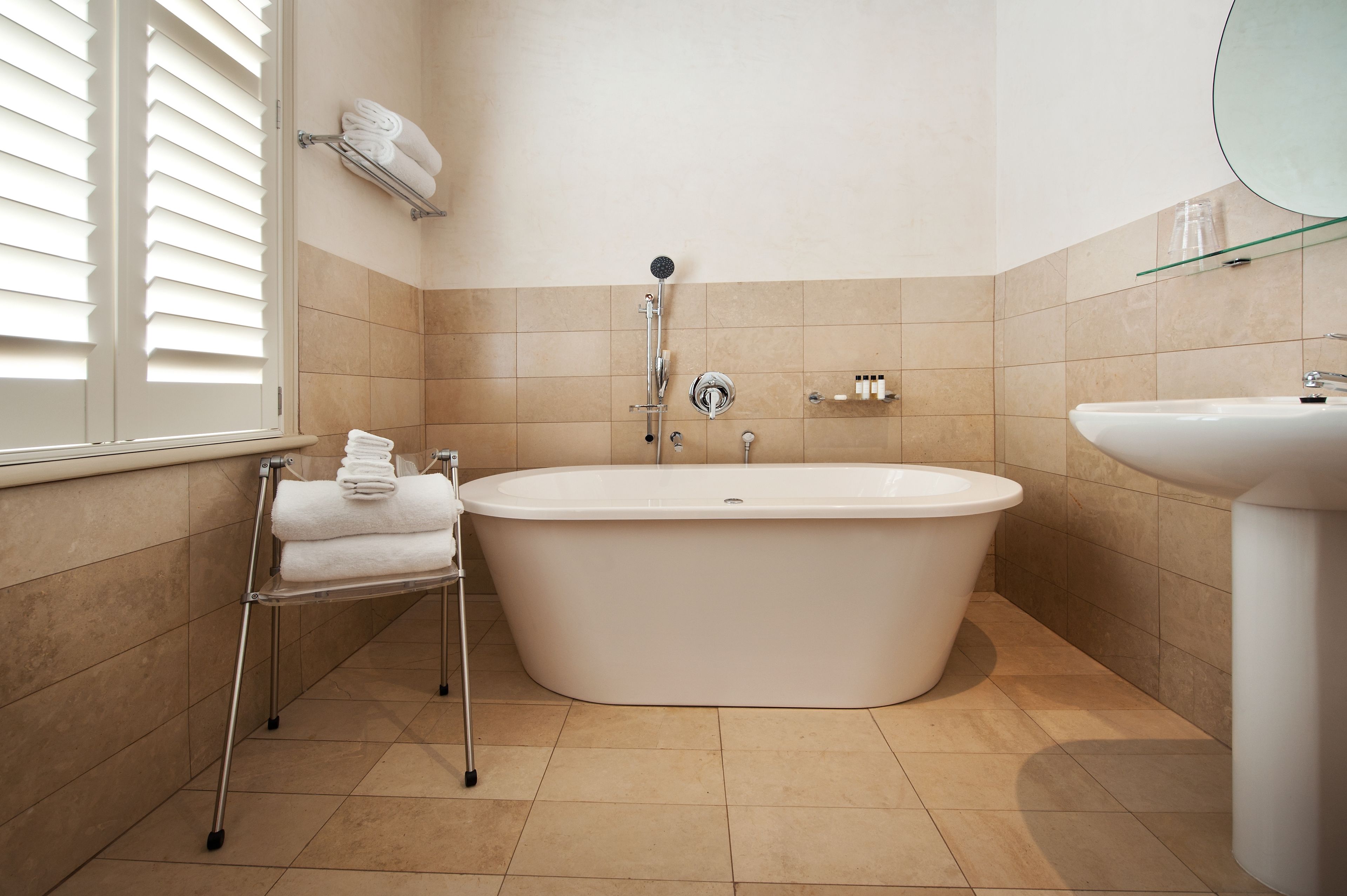 Un baño moderno con una bañera independiente, un lavabo y un estante de vidrio con toallas.