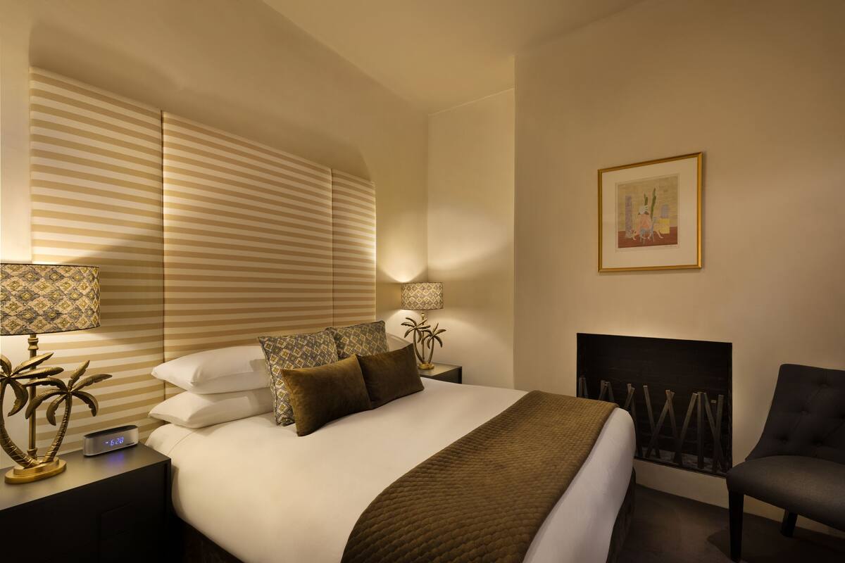 A hotel room with a large bed, a nightstand with a lamp, a chair, and a painting on the wall.