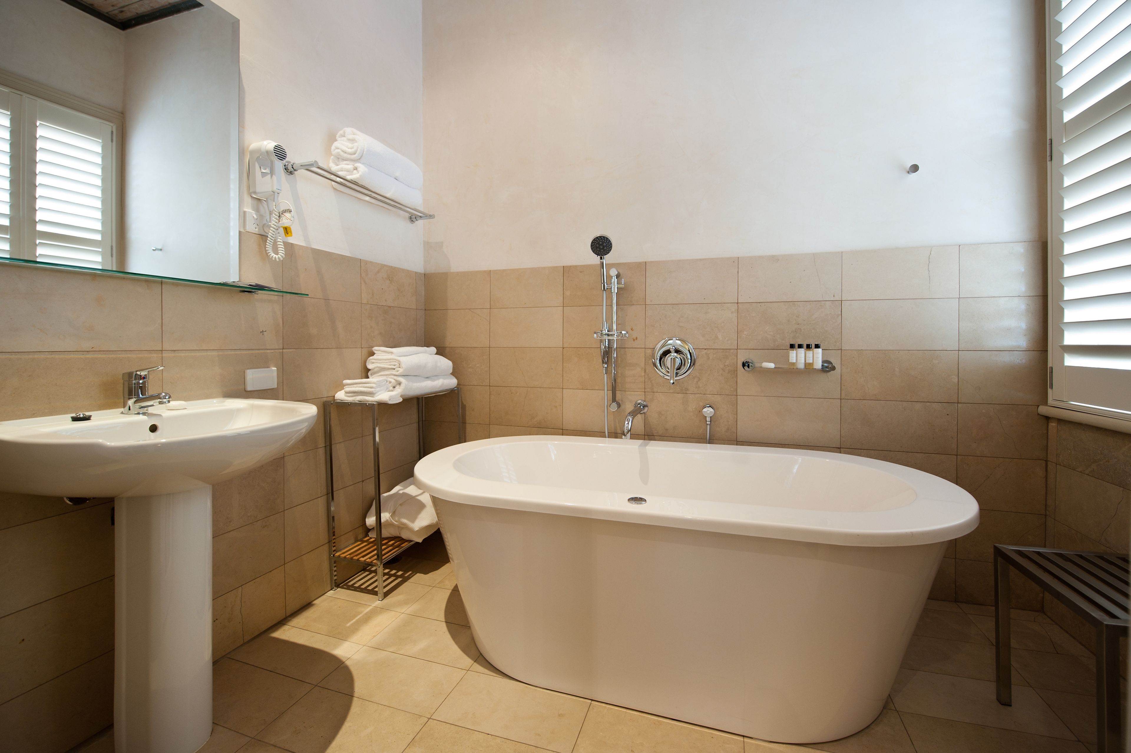 Un baño moderno con una bañera independiente, un lavamanos pedestal y un estante de vidrio con toallas.