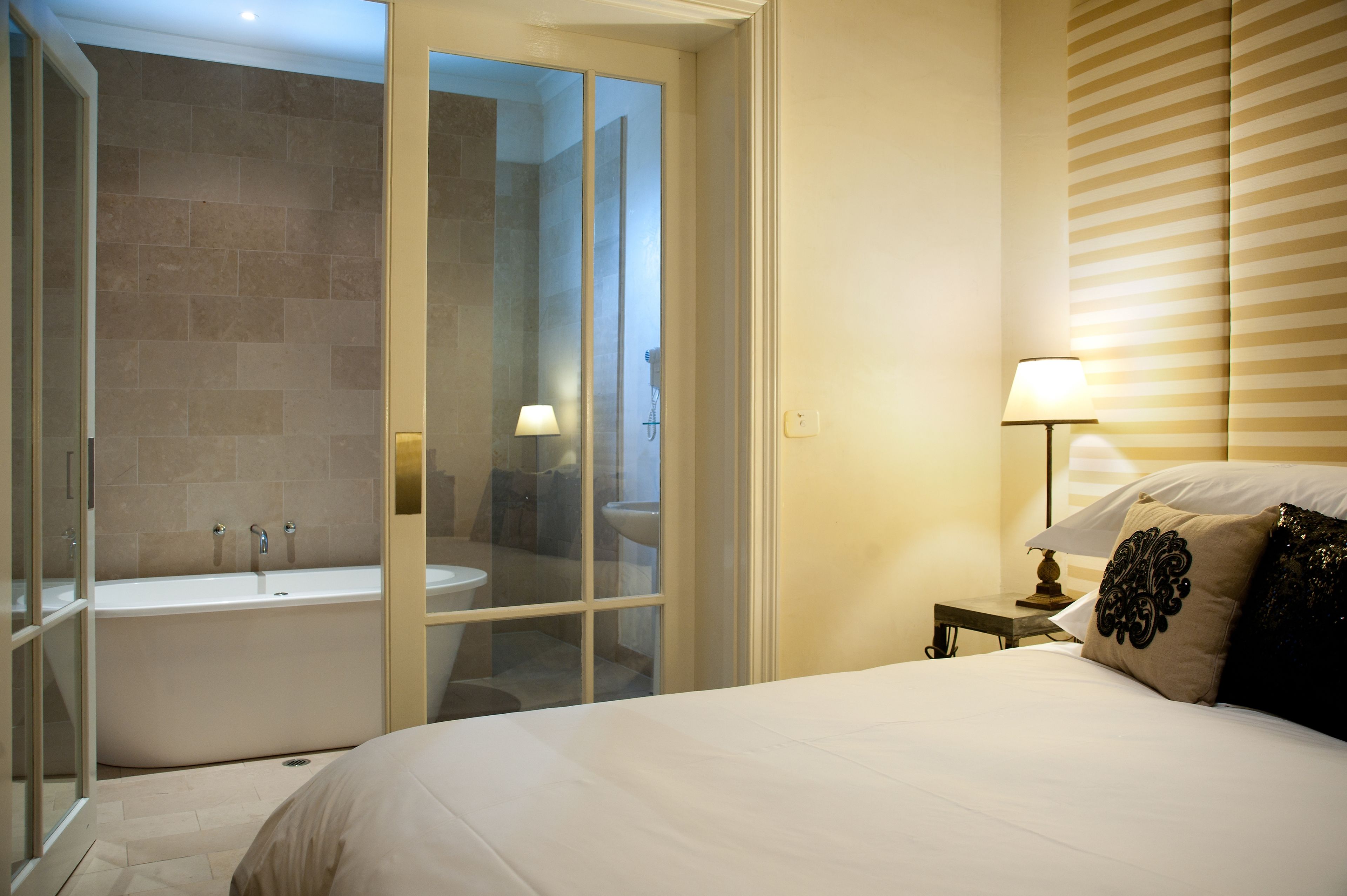 A hotel room with a large bed, a bathroom with a bathtub, and a nightstand with a lamp.