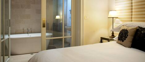 A hotel room with a large bed, a bathroom with a bathtub, and a nightstand with a lamp.