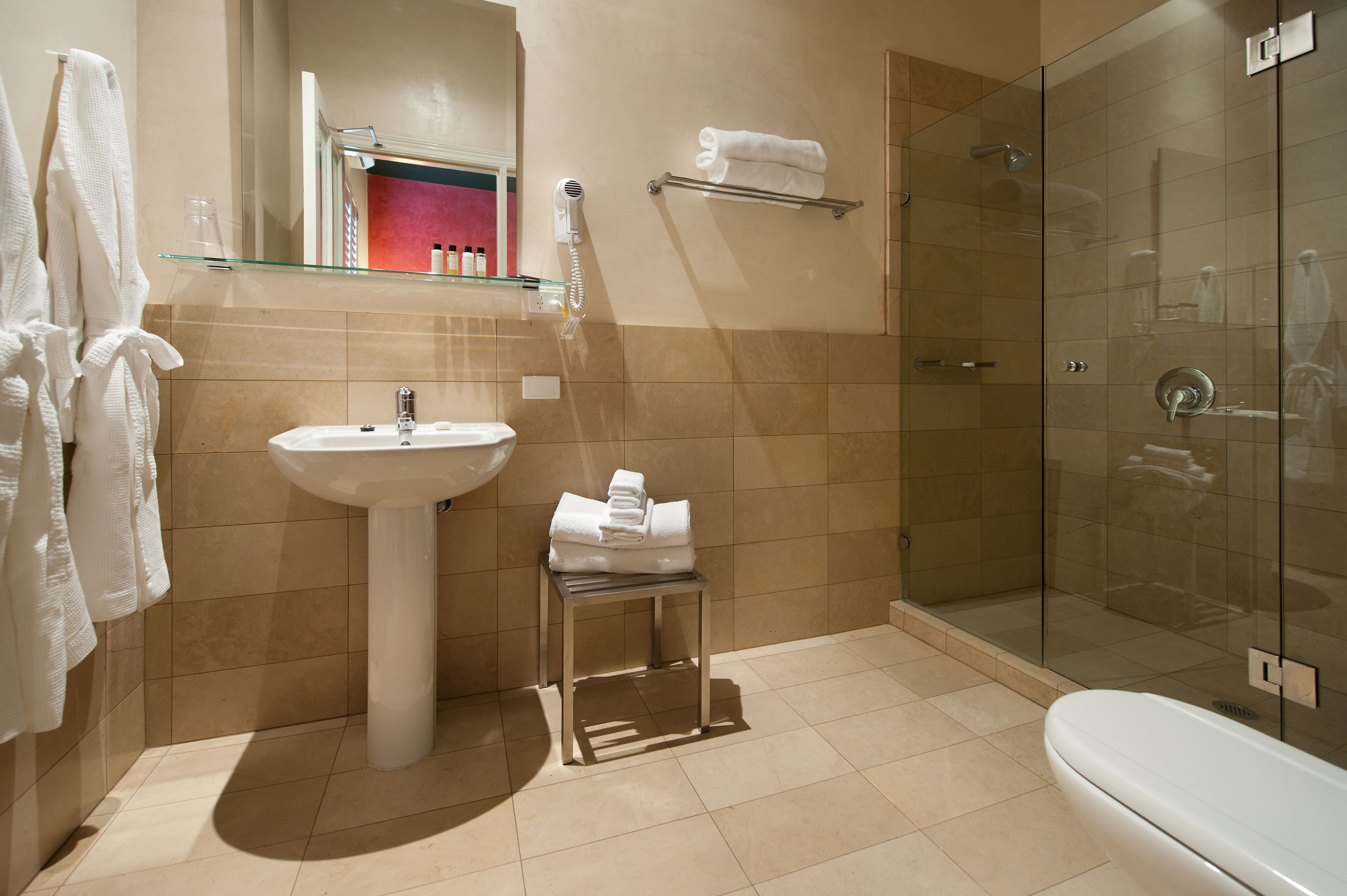 A modern bathroom with a glass shower enclosure, a pedestal sink, and a glass shelf above the sink.