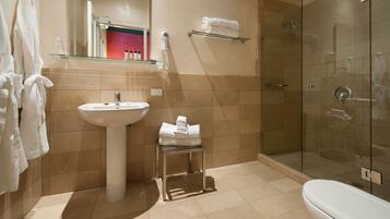 A modern bathroom with a glass shower enclosure, a pedestal sink, and a glass shelf above the sink.