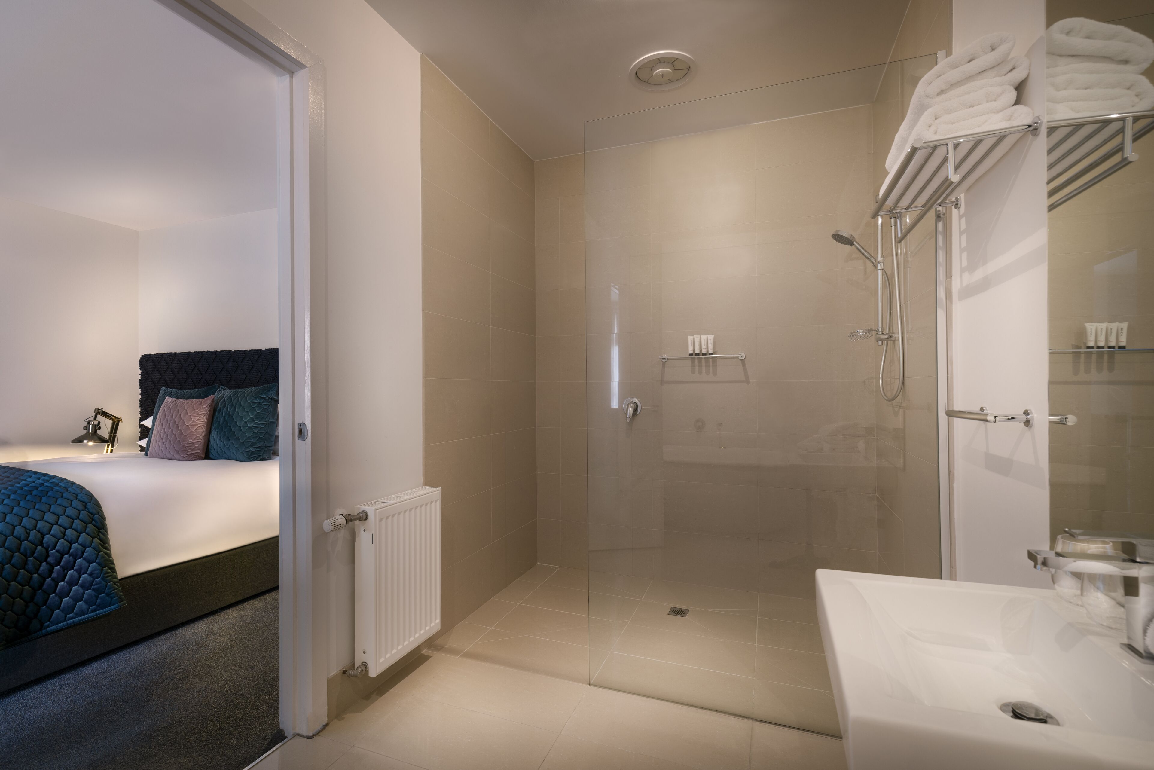 Un baño moderno con ducha envuelta en vidrio, lavamanos blanco y un perchero para toallas ordenado.
