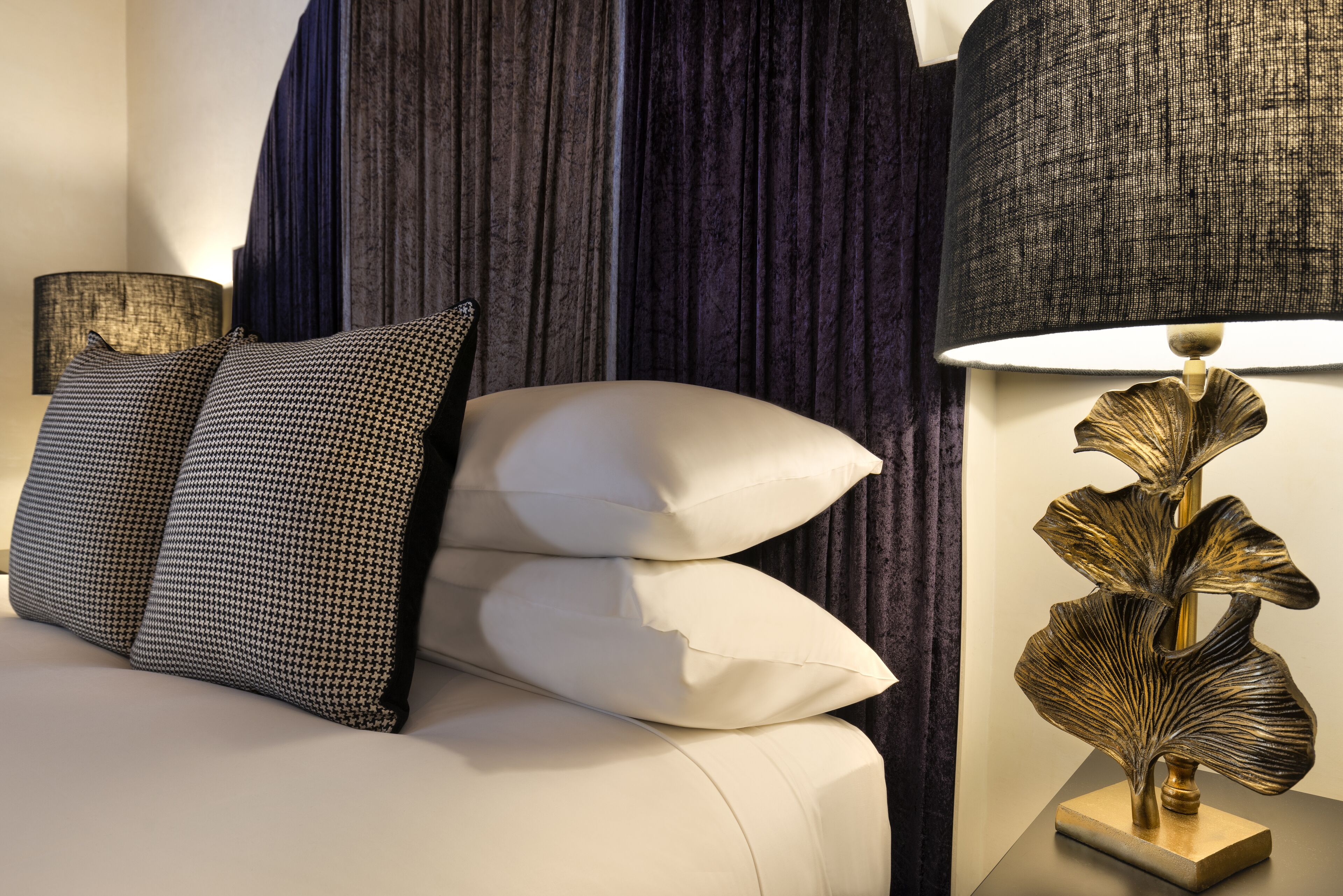 A bed with patterned pillows, a decorative lamp, and dark curtains.
