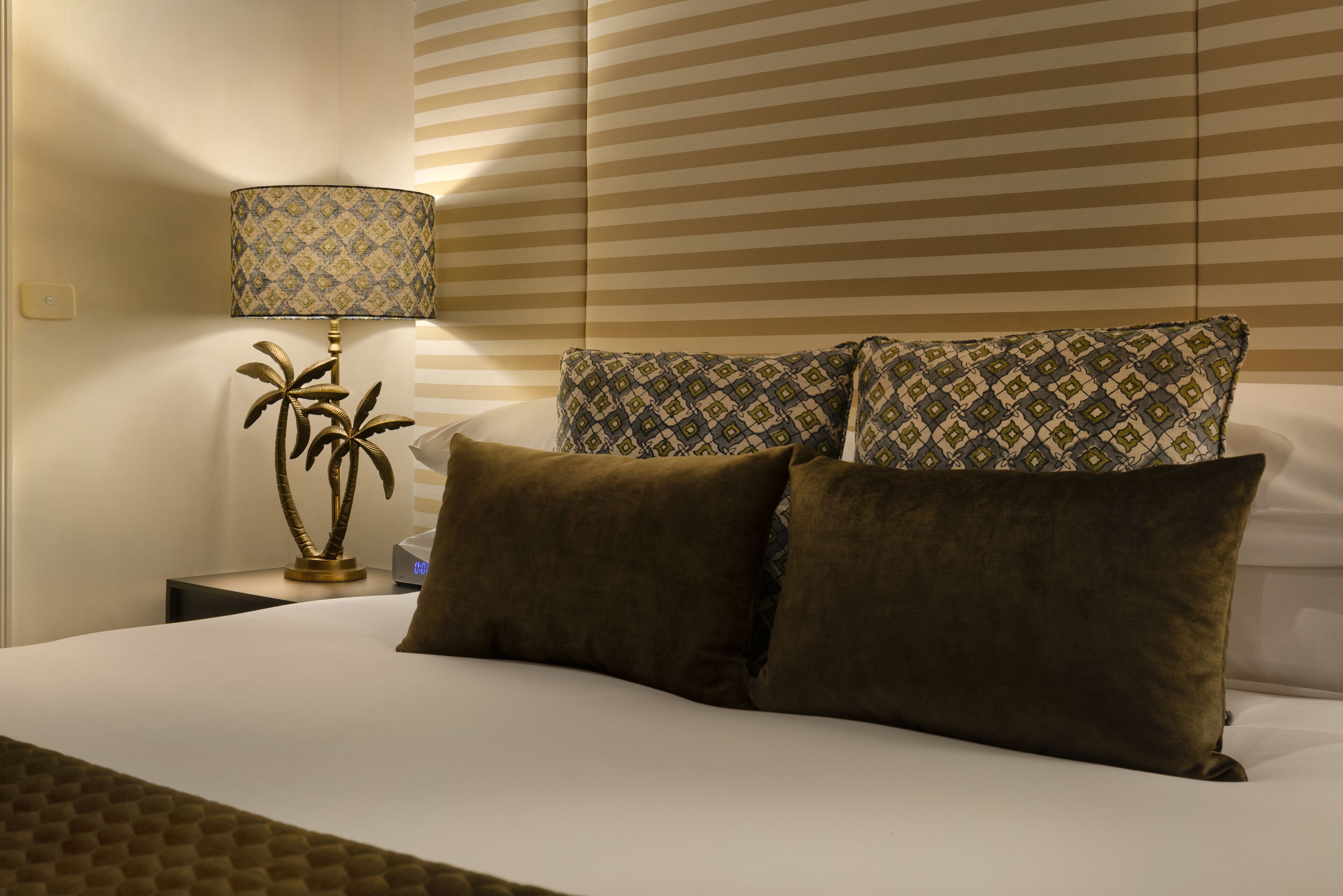 A hotel room with a bed, a nightstand with a lamp, and a wall with striped wallpaper.