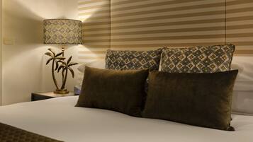 A hotel room with a bed, a nightstand with a lamp, and a wall with striped wallpaper.