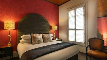 A bedroom with a large bed, two bedside tables with lamps, a chair, and a window with blinds.